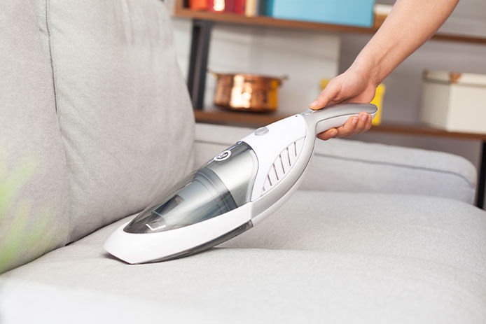 A person hand vacuuming a couch