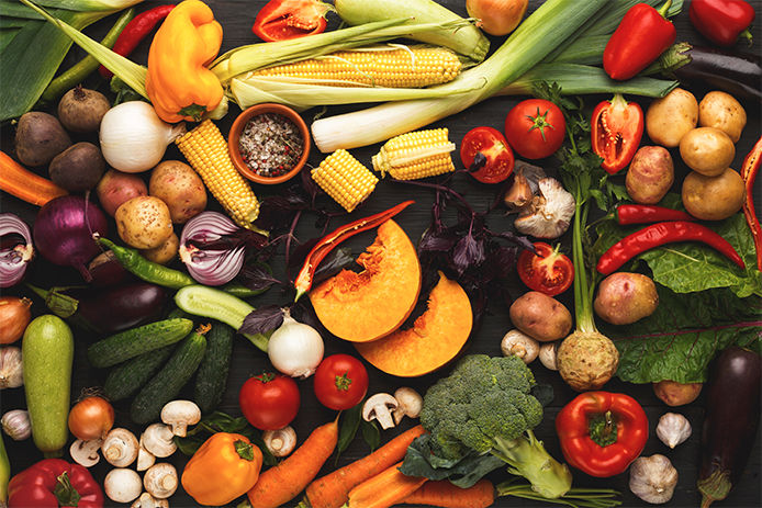 A colorful overhead shot of a variety of fall vegetables including corn, squash, carrots, peppers, mushrooms, onions, leaks, tomatoes and potatoes