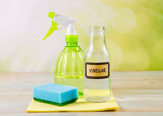 An image of home cleaning products including a spray bottle, vinegar, and a sponge