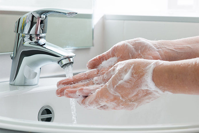 A close up of a person washing their hands under a bathroom faucet. Their hands are covered in soap and bubbles and the water is running 