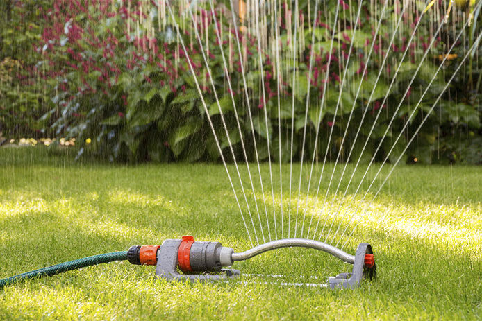 A red and grey sprinkler watering a green and healthy lawn