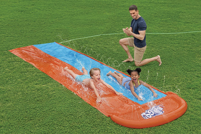 Kids playing on a slip and slide outside in the grass