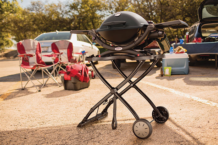 The Weber Q Series grill and grill stand in a parking lot tailgating 