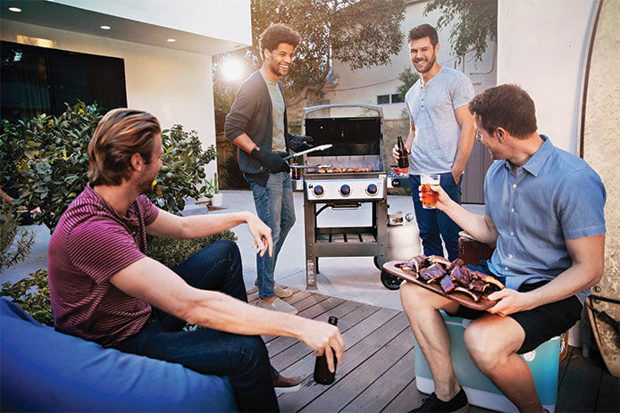 A group of four guys sitting out on a patio around a Weber Spirit Gas grilling BBQing 