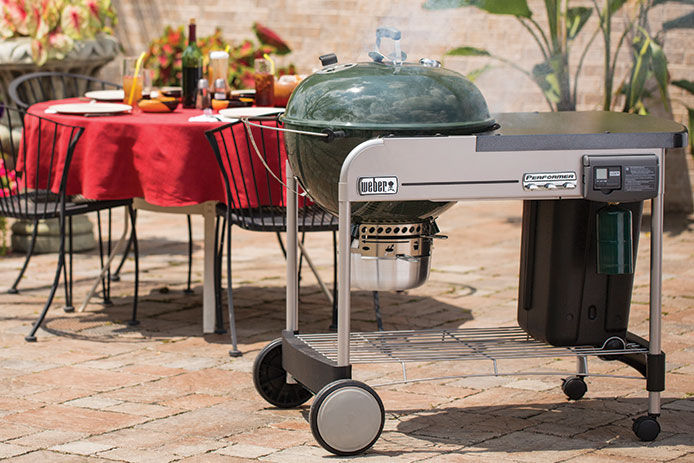 A green Weber Performer Grill sitting on a patio with patio tables behind it 