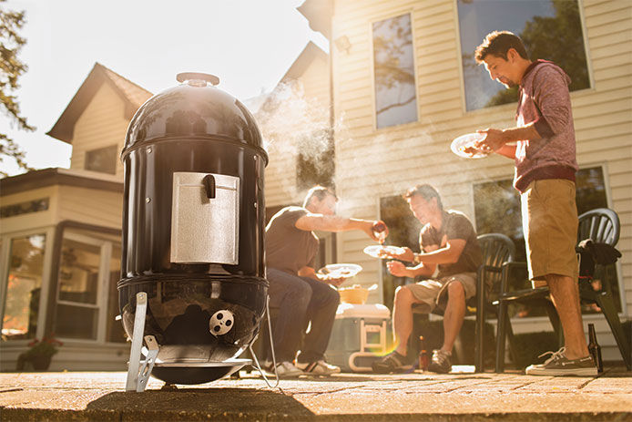 A lifestyle image of a Weber smoker being used during a house party