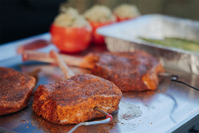 Steaks cooking on a flattop grill with a meat thermometer stuck in the side of one of the steaks