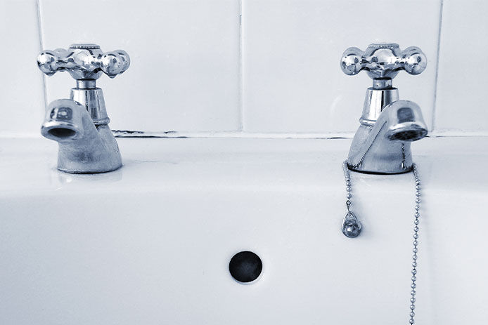 Two silver taps on a white sink with a plug on a chain