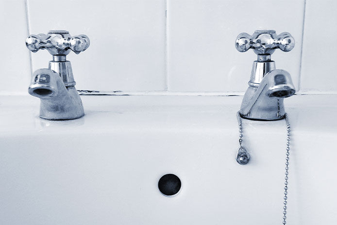 Two silver taps on a white sink with a plug on a chain