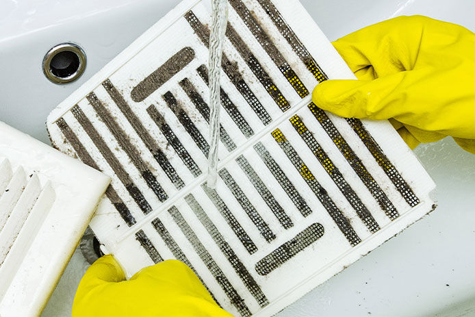 Person in a protective rubber glove washes in the sink air filter of the ventilation return duct blocked by dust and debris. Cleaning service.