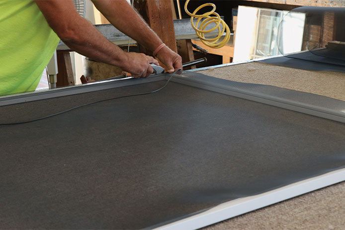 A man wearing a high vis green shirt repairing a window screen in his garage