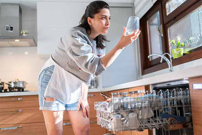 Young woman takes a glass out of the dishwasher in kitchen.