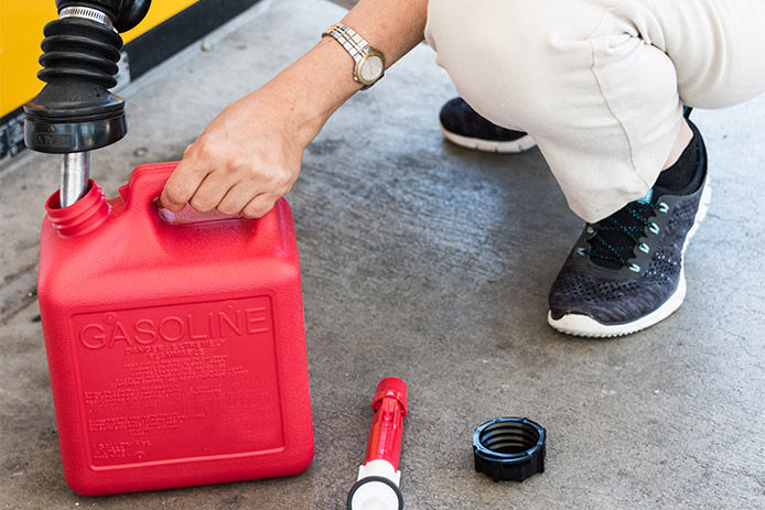 An image of a person filling up a gas can at a gas station on the cement ground