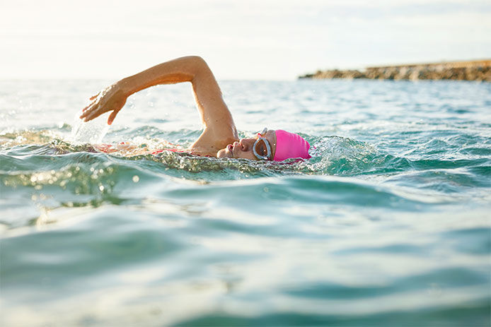 Determined senior woman swimming in sea. Confident swimmer is wearing swimming goggles and cap. Female is representing her healthy lifestyle.
