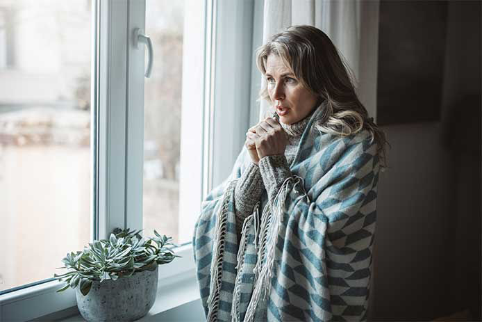 A cold woman standing by a window