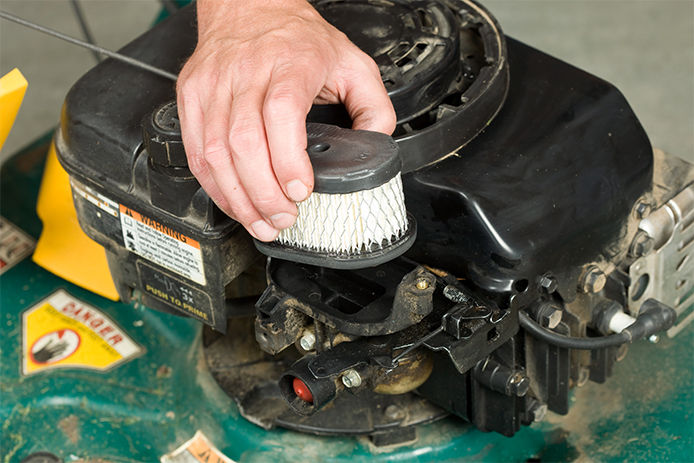Man replacing old air filter in lawn mower for a new one, close-up
