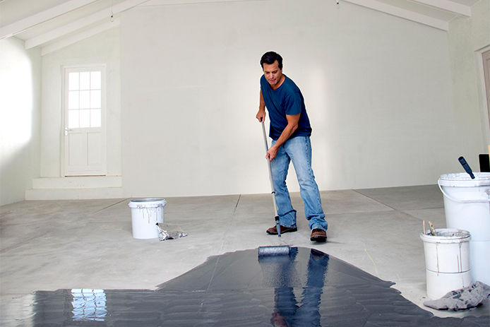 Applying RockSolid Floor coating by Rust-Oleum. The man shown is using the silver floor coating, applying it with a paint roller 