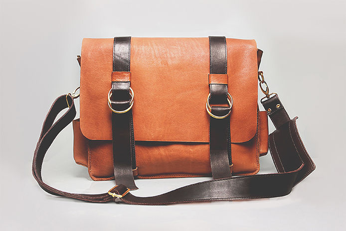 A tan leather bag with black straps and silver clapses