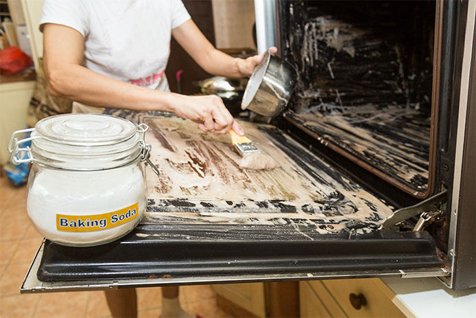 Woman using a baking soda mixture to clean the inside of oven door