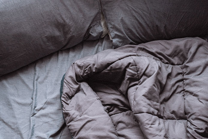 A crumpled up gray comforter on a queen size bed