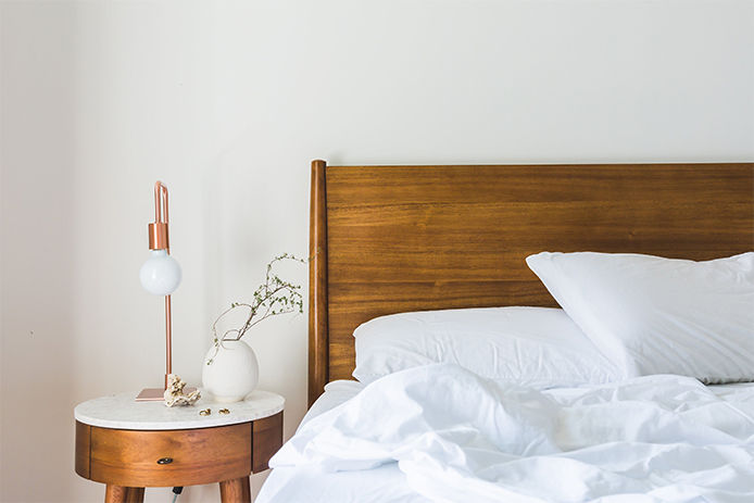 A close up image of a clean looking bedroom with white sheets and a wooden side table