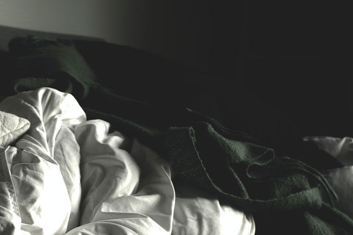 A black and white image of blankets/comforters wrinkled up on a bed.