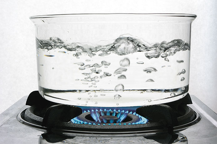 A glass pot of bowling water on a burner