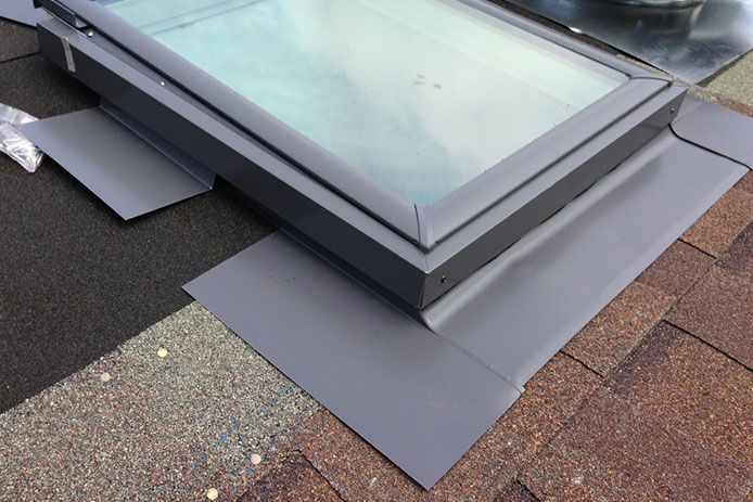 Attaching flashing to the bottom of a newly installed skylight on a shingled rooftop 