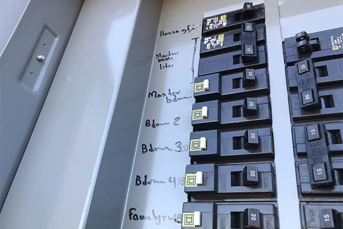 A grey home electrical panel of a circuit breaker box holds black switches that can control the power source to any room or set of electric outlets in the home.