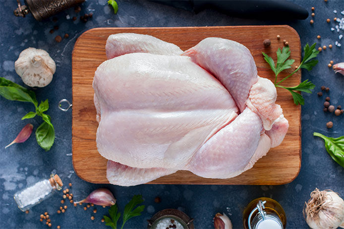 Clean, uncooked turkey on a wooden cutting board with garnishes surrounding on countertop