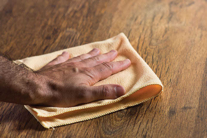 Person using a yellow microfiber cloth to dust wooden tabletop