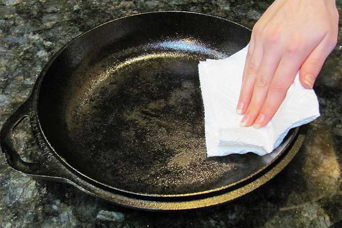 Person wiping down their brand new skillet with a paper towel
