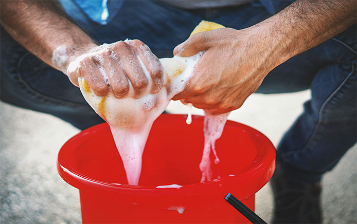 Man squeezing soapy water out of sponge into a red bucket