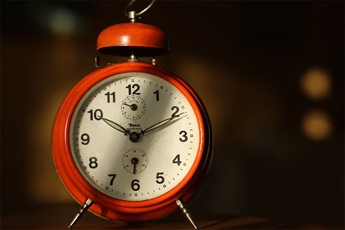 A close up image of a red clock with the hands at 10:11. The background is dark and blurred out 