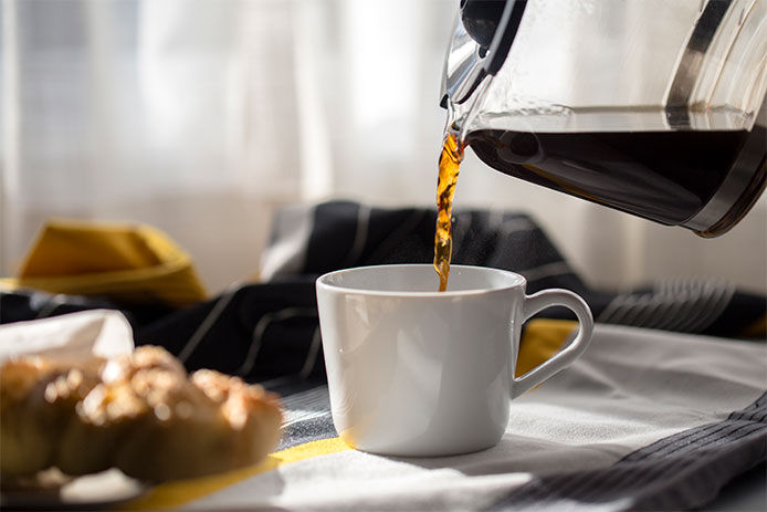 Pouring black coffee into white coffee mug