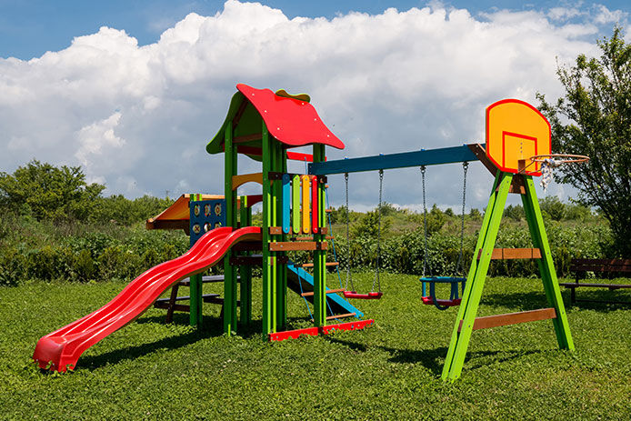 A very colorful playground set with two swings, a slide, and a basketball hoop