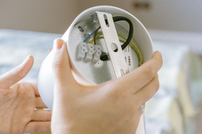 Person holding a white light fixture looking at the wiring on the back