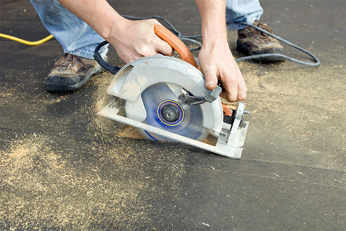A man using a circular saw to cut through the rooftop of a residential home