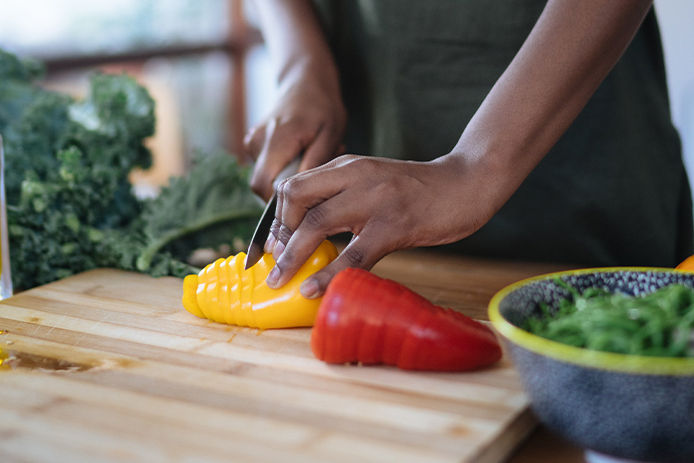 A women chopping yellow and red peppers on a wooden cutting board with greens and olive oil surrounding her table