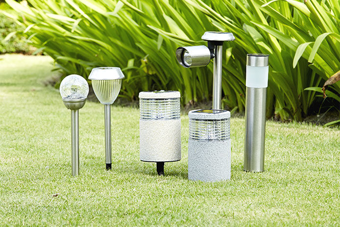 A variety of solar and wired lights for landscaping displayed on a grassy lawn in front of landscaping 
