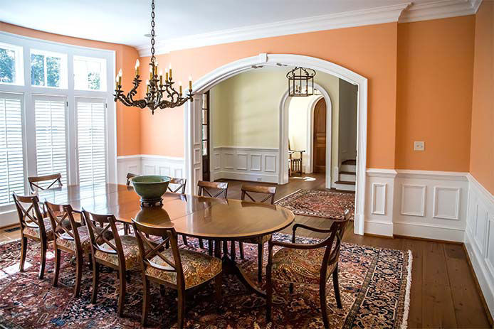 Orange peach colorful dining room with oriental rug and classic wood chairs and table with chandelier and artwork.