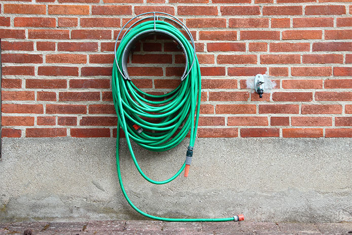 a green garden hose wound up on a garden hose reel disconnected from the spigot
