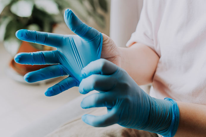 A person putting on blue latex gloves before working with harsh chemicals 