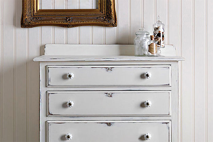 A chalk white dresser with three glass containers on top of the dresser