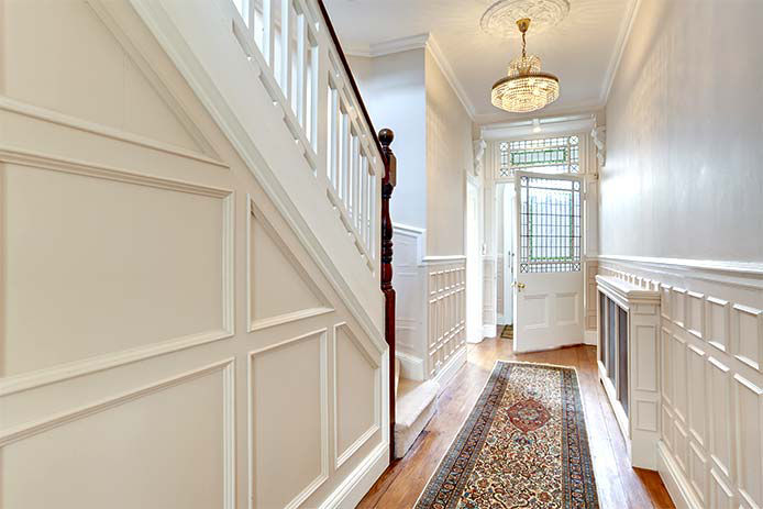 Reception hall to period victorian property decorated in white and cream with chandelier, stairs and glazed panelled door.