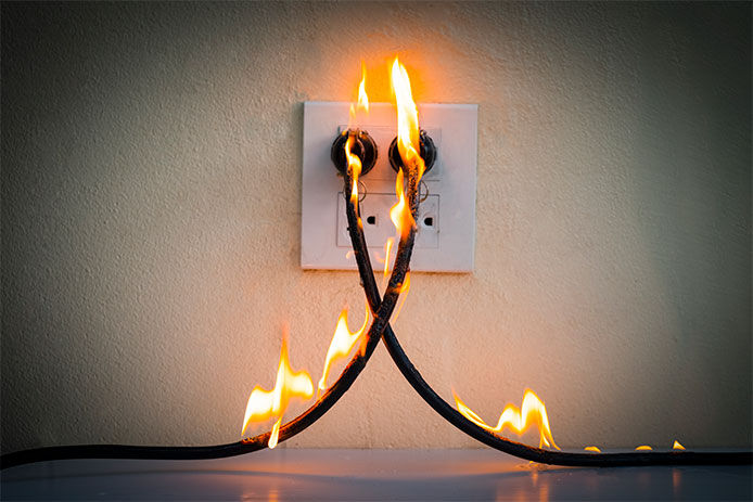 Extension cords plugged into a wall outlet that are on fire