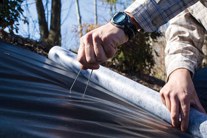 Person sticking ground staples into the landscaping fabric to hold in place, close-up