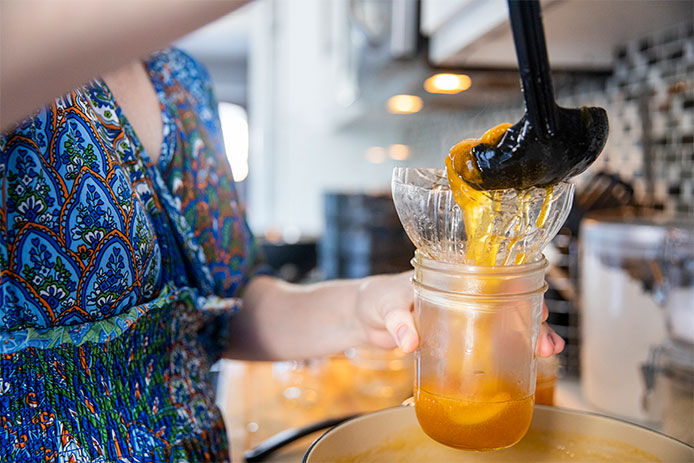 Woman using a ladel to pour the fruit into glass canning jar