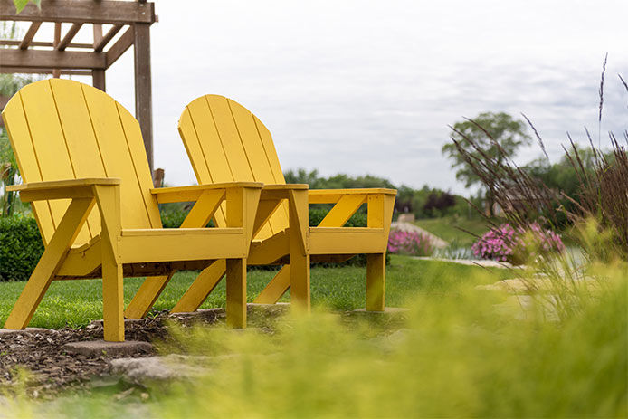 Spring garden with two bright yellow wooden adirondack chairs 
