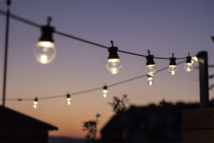A close up image of back patio string lights glowing in the evening sky 